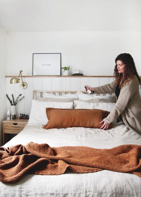 woman spraying linen spray on pillows on bed