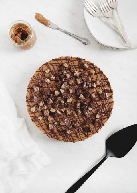 no bake peanut butter cheesecake with chopped peanut cups and drizzled chocolate on it with jar of peanut butter