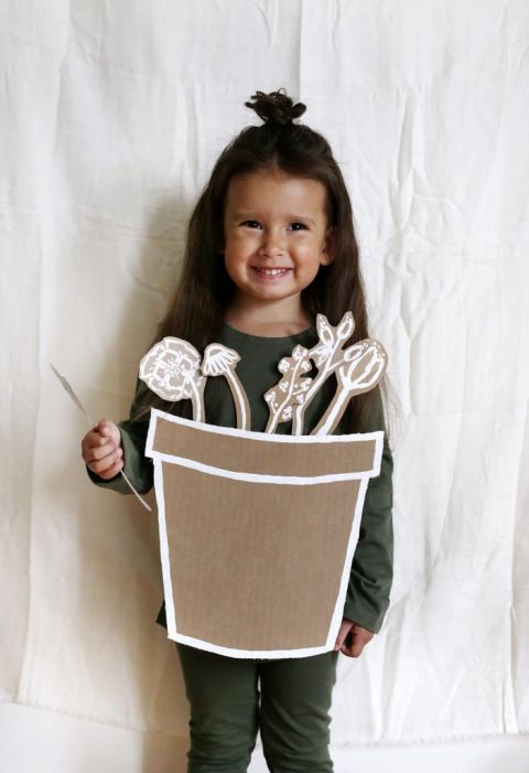 little girl in green clothes and a cardboard flower pot costume