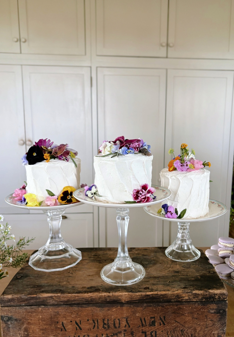 three small cakes on cake stands decorated with edible flowers