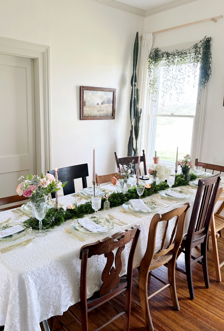 table setting for floral bridal shower with moss on table and greenery hanging in window behind table