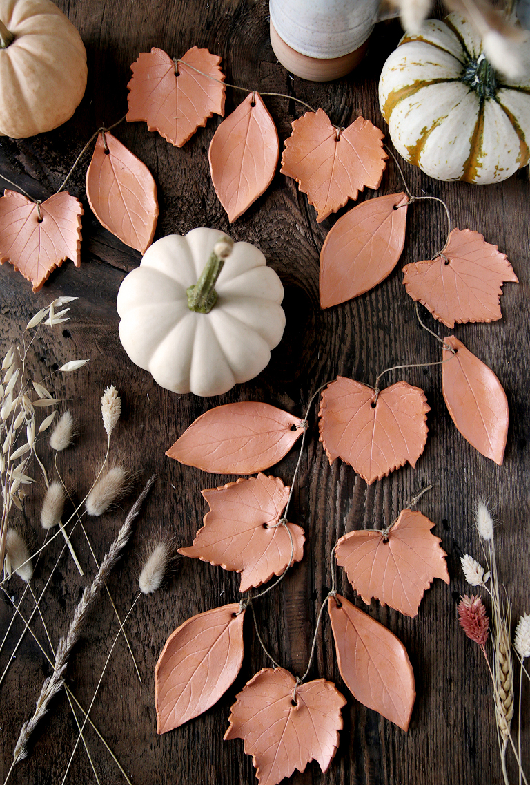 diy clay leaf garland with twine laying on wood board with mini pumpkins around it and dried grass next to it