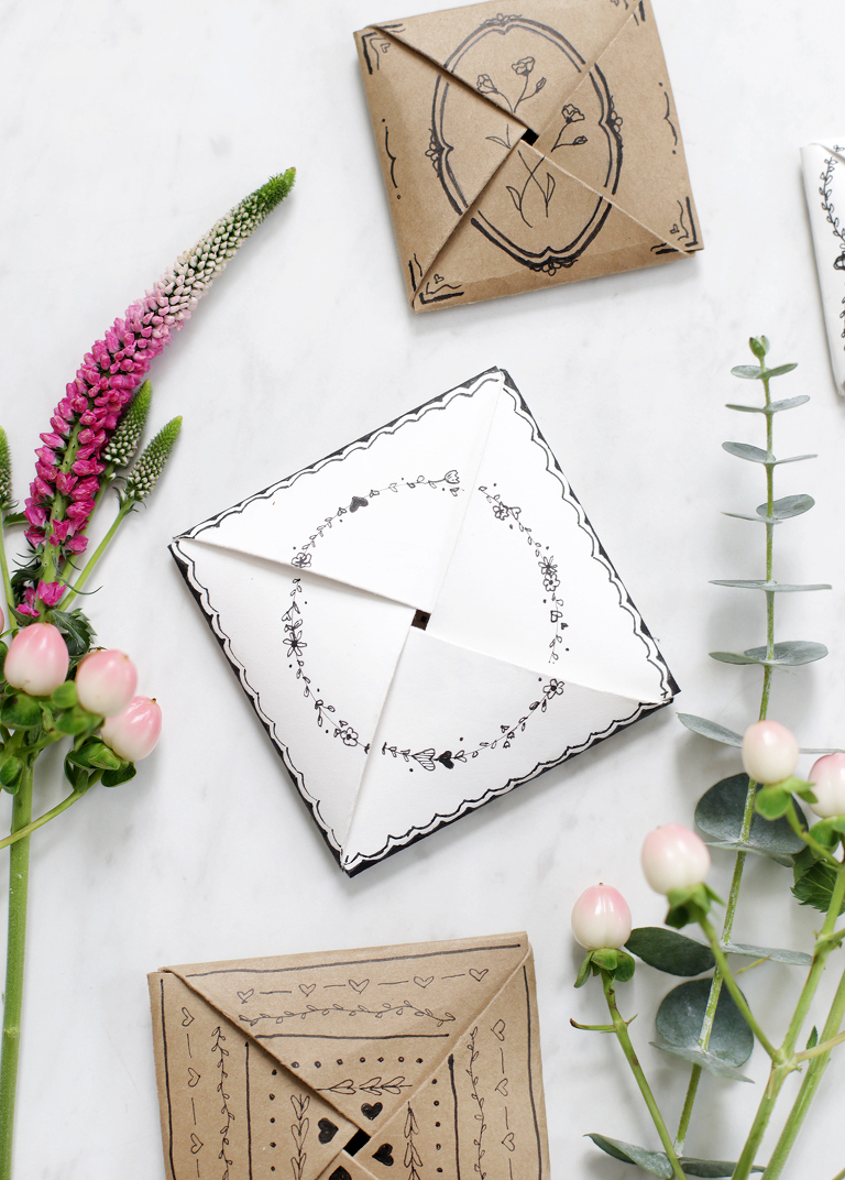 mini folded paper cards with black floral doodles next to fresh flowers