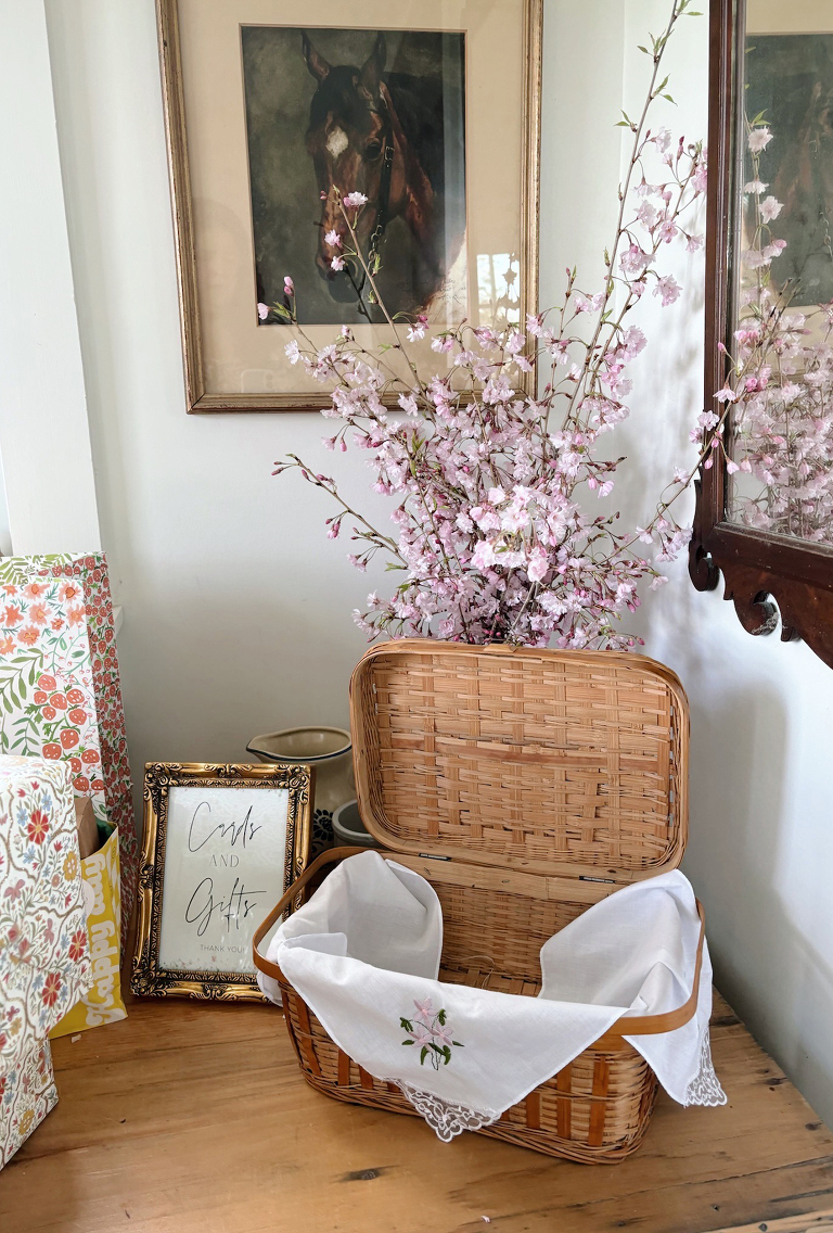 shelf with cards and gifts for bridal shower with basket for cards and pink cherry blossoms behind basket