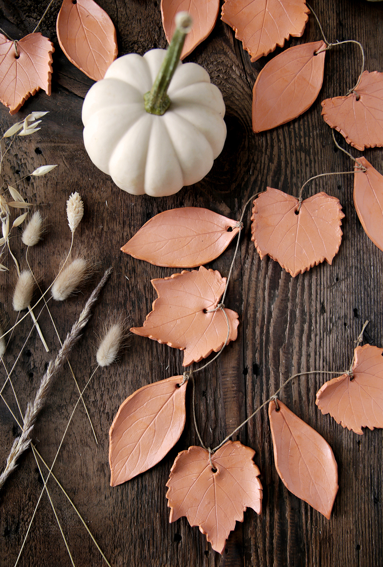 terracotta leaf garland on wood board with white mini pumpkin and dried fall grass next to it