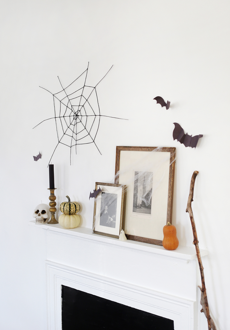 fireplace mantel with frames, pumpkins and surrounded by black bats on wall and black string spider web