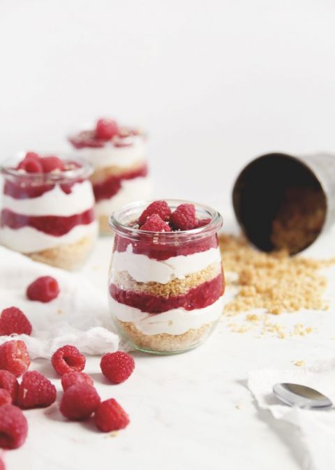 glass jars of no bake raspberry cheesecake parfait next to raspberry and crumbs
