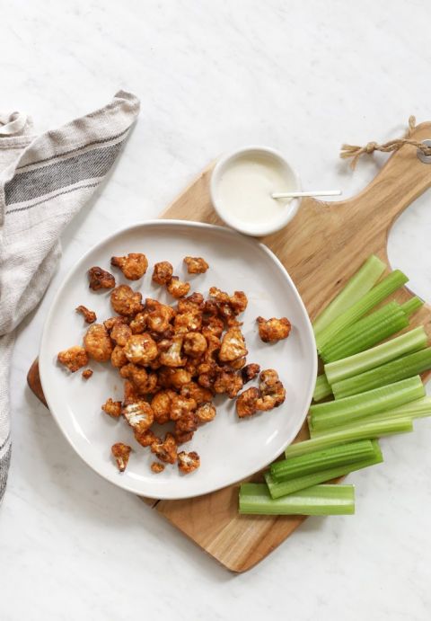 buffalo cauliflower on white plate with celery and blue cheese beside it