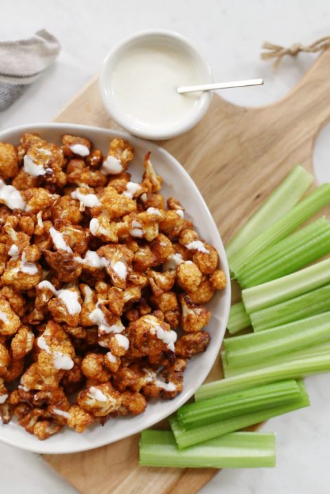 plate of buffalo cauliflower on a cutting board surrounded by celery and dressing