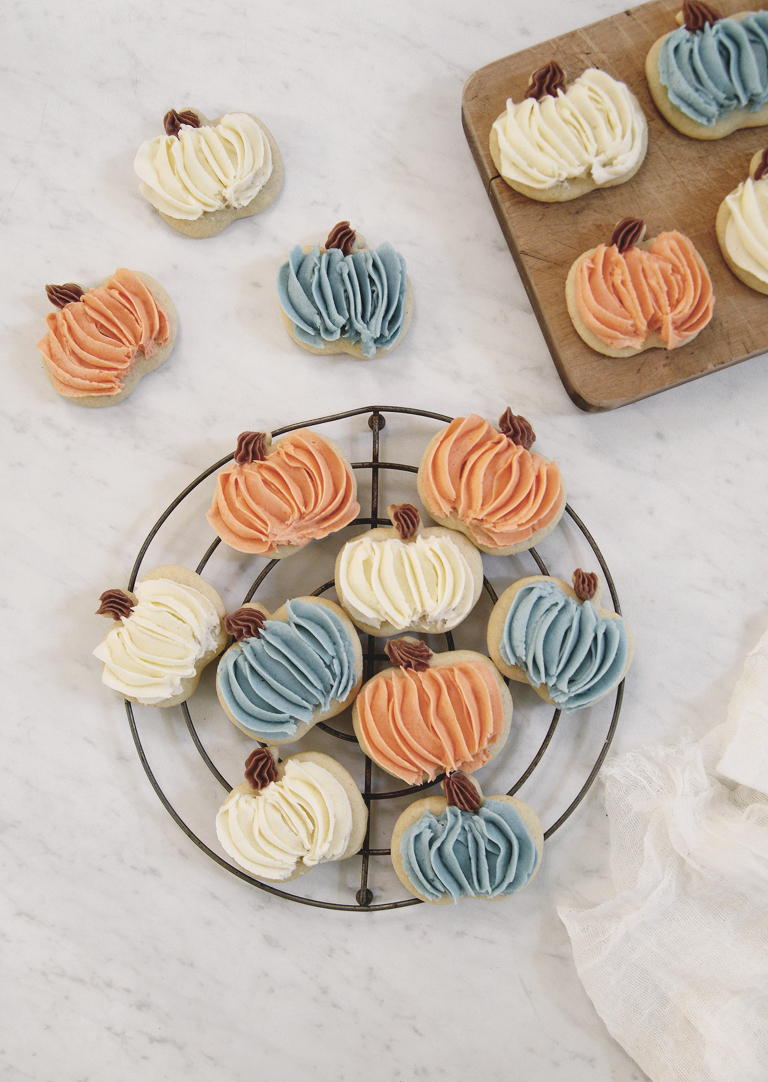 pumpkin cookies with orange, blue, and white frosting on cooling rack and wood cutting board