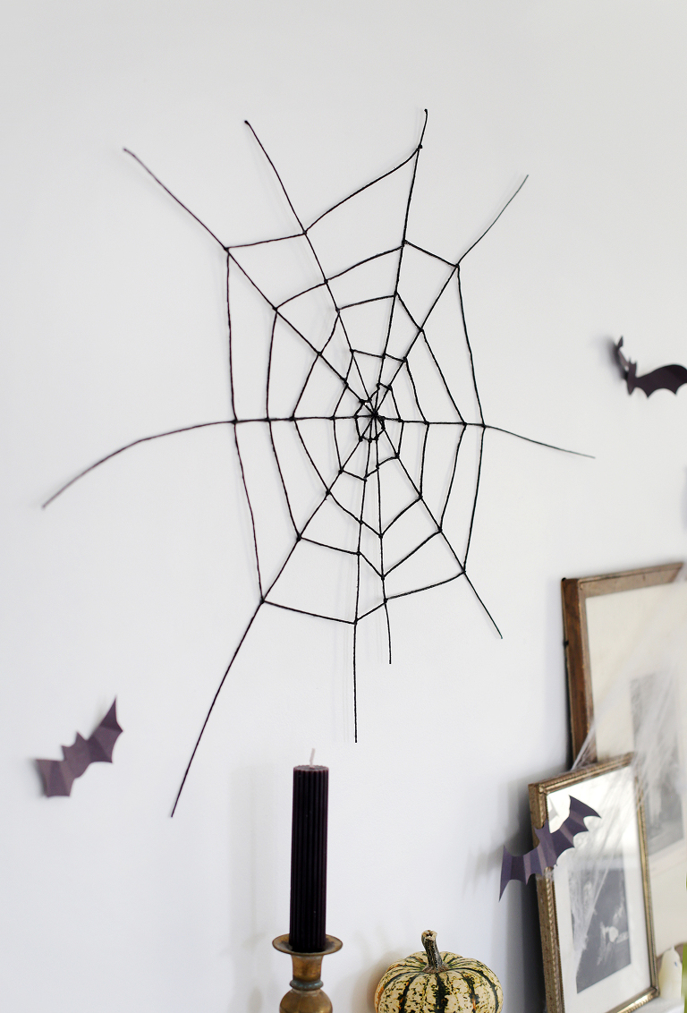 black spider web on wall next to cut out bat and vintage frames and black candle