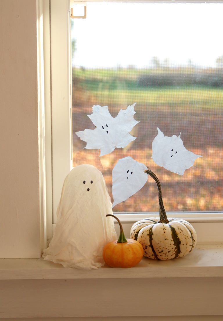 white window sill with cheesecloth ghost and mini pumpkins on it with window cling glue ghosts on window