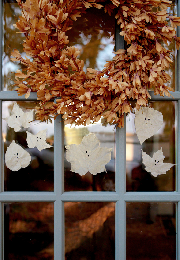 blue window panes with fall wreath hanging on it and transparent glue leaf ghosts hanging on window
