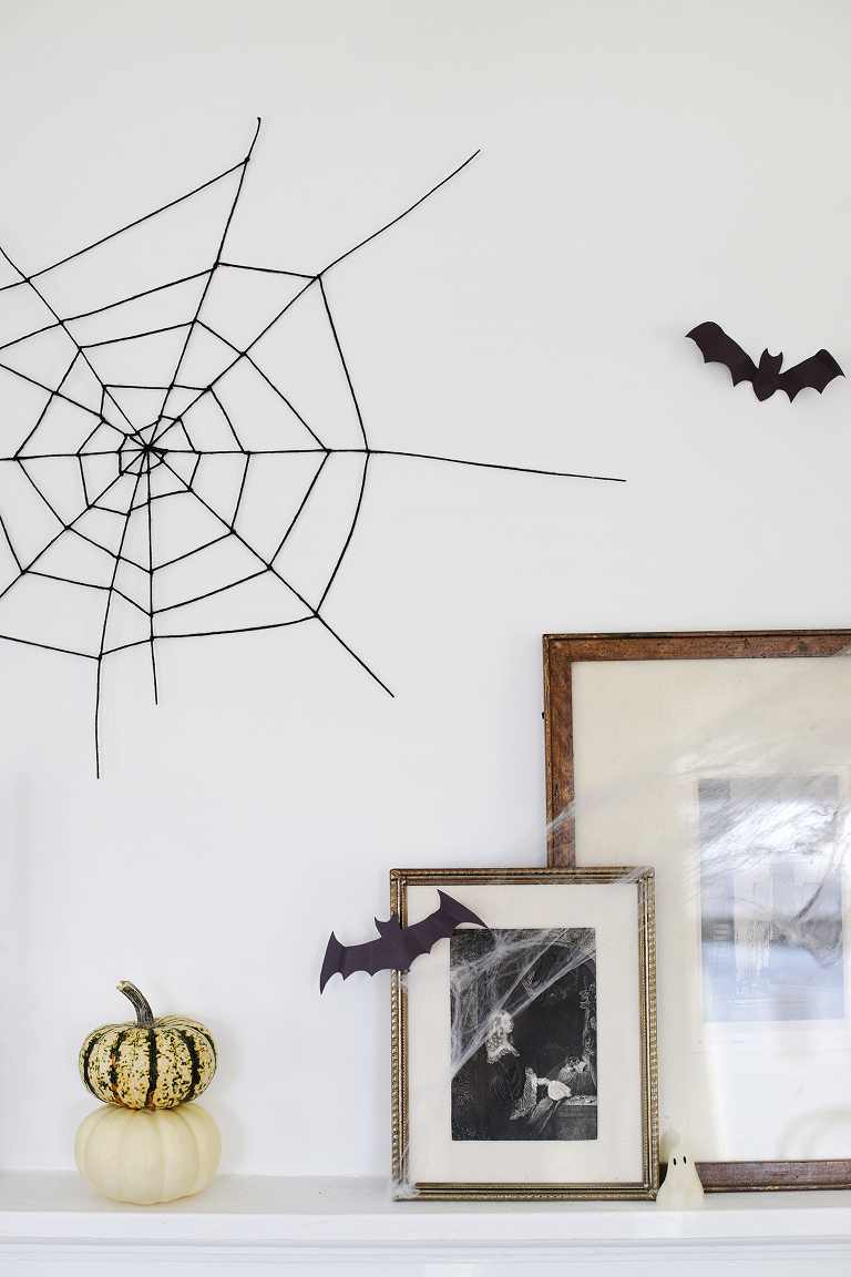 black spider web on wall next to cut out bat and vintage frames