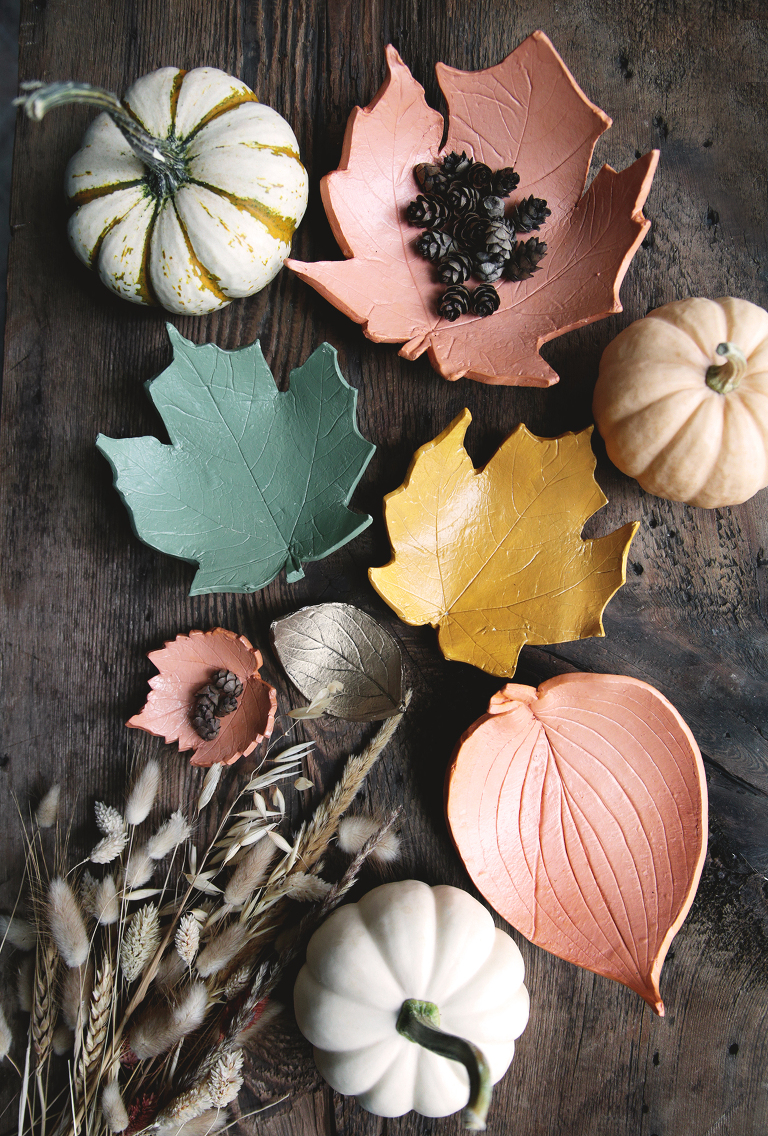 arrangement of clay leaf bowls and mini pumpkins on wood board with dried grass in the corner
