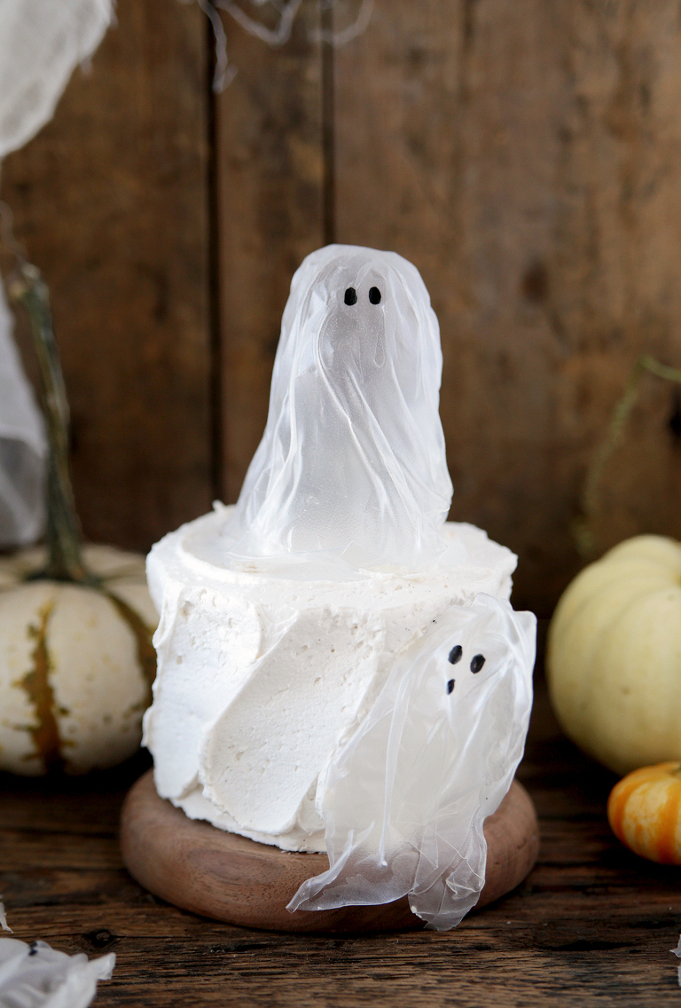 small white cake with ghost decorations on cake and mini pumpkins in background