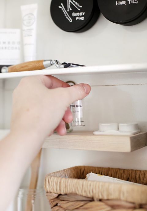 hand grabbing dental floss off small wooden shelf inside white medicine cabinet