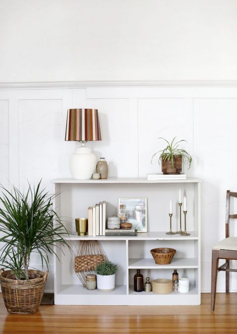 shelf against white wall styled with books and plants and candles