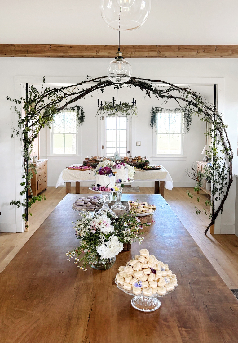 room with grapevine branches and greenery around archway with desserts and food set on tables in the room