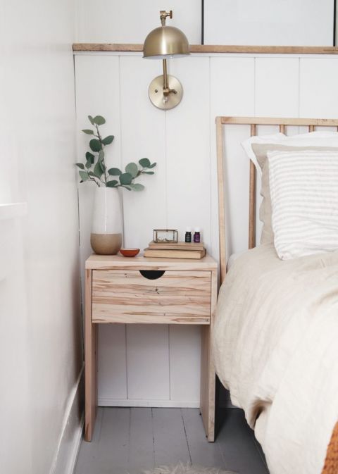 wood nightstand with brass lamp next to a bed