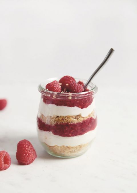 glass jar filled with layers of crust, cheesecake filling raspberry filling