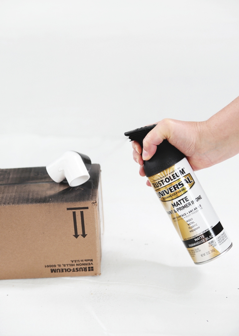 can of black spray paint spraying white corner elbow