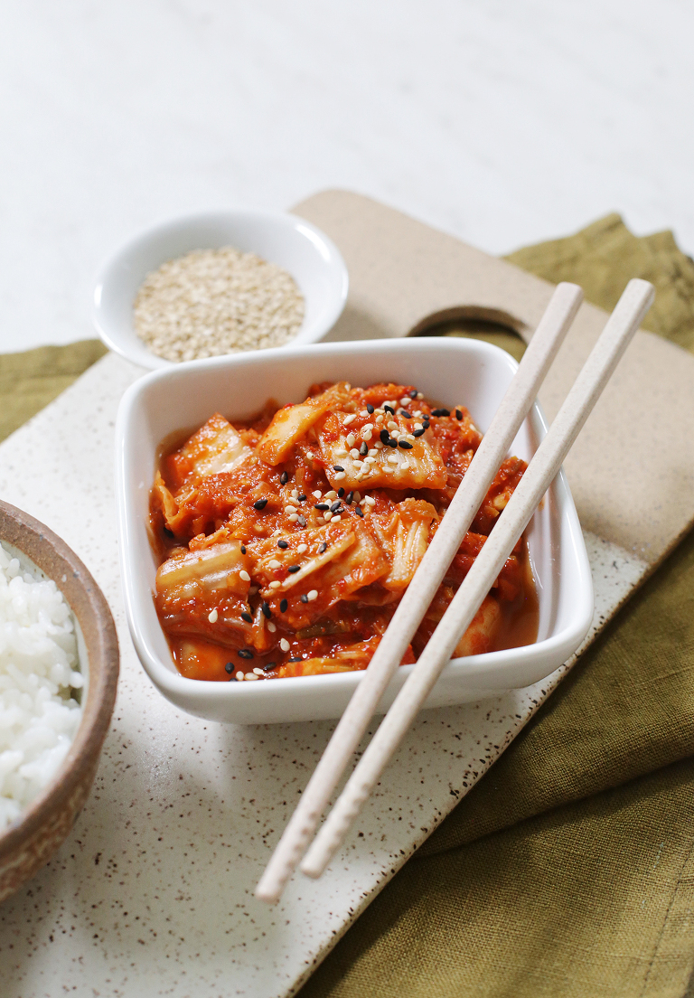 square white bowl filled with kimchi with chopsticks resting across top of bowl