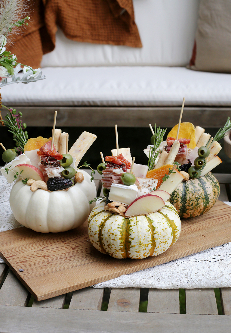 three individual charcuterie boards arranged inside carved out mini pumpkins