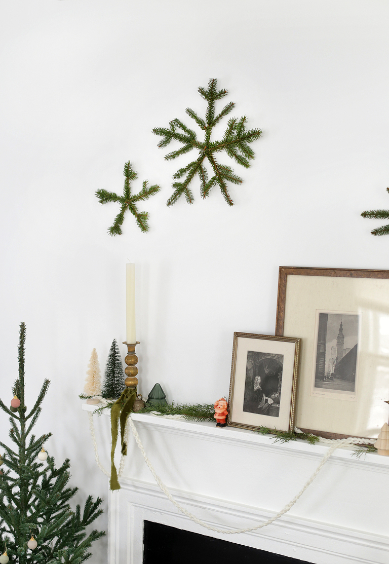pine snowflakes on white wall above christmas decorated mantle and mini christmas tree