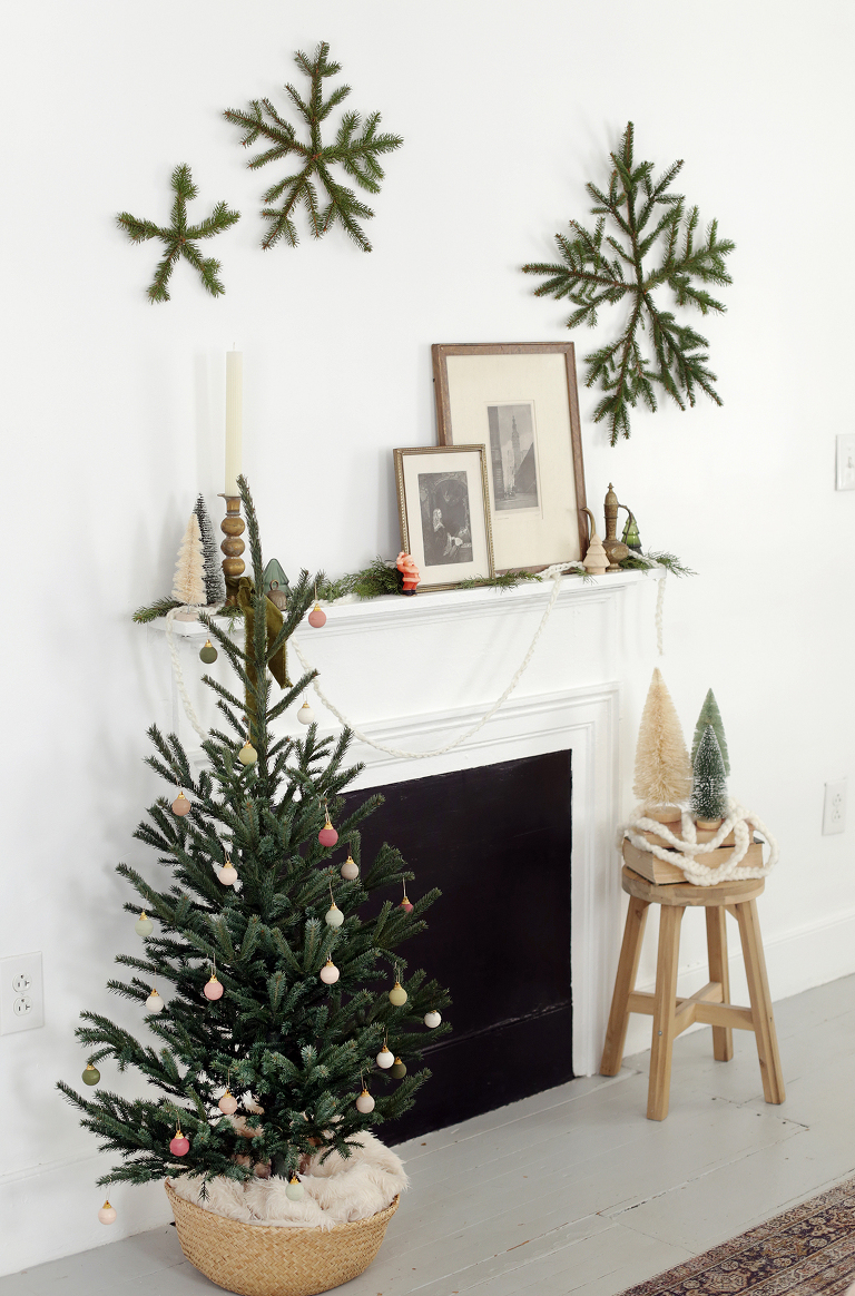 mantle with christmas decor and vintage frames, small tree beside it, pine snowlfakes hanging on the wall