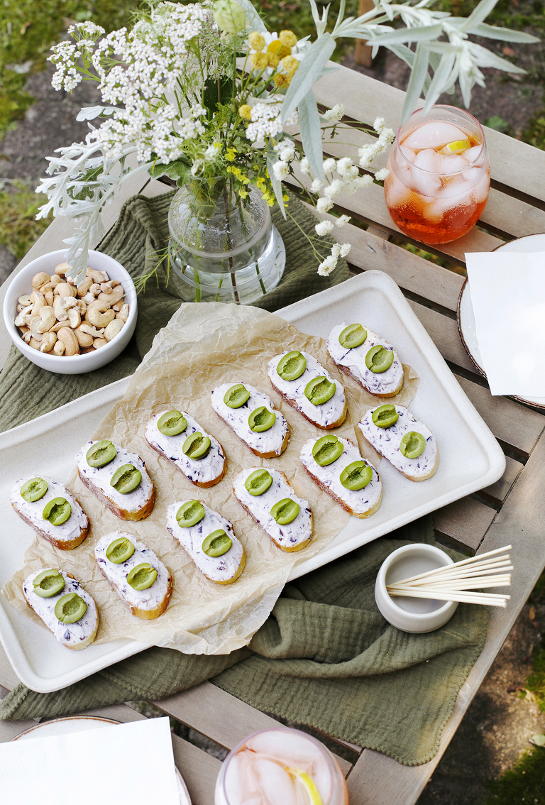 ceramic tray of crostini on wooden table with green kitchen towel and vase of flowers