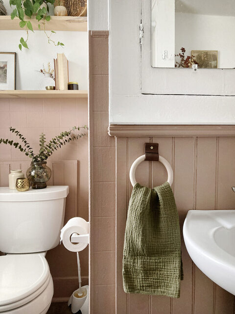 wooden towel ring against brown pink wall next to white pedestal sink