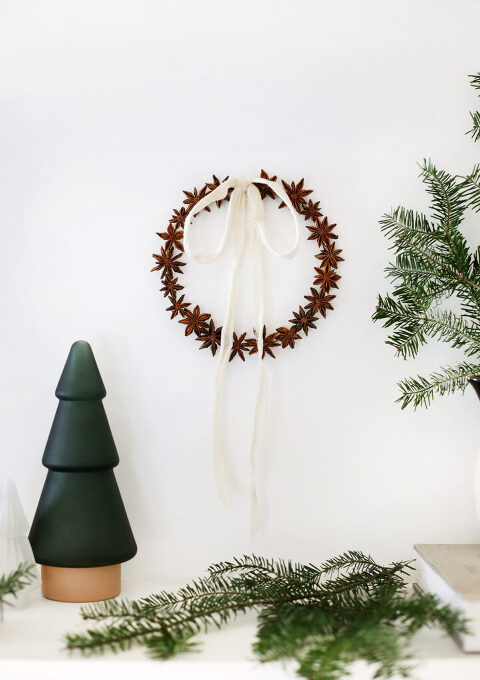 small star anise wreath with surf fabric bow hanging on white wall next to fresh pine workshop and christmas tree decor