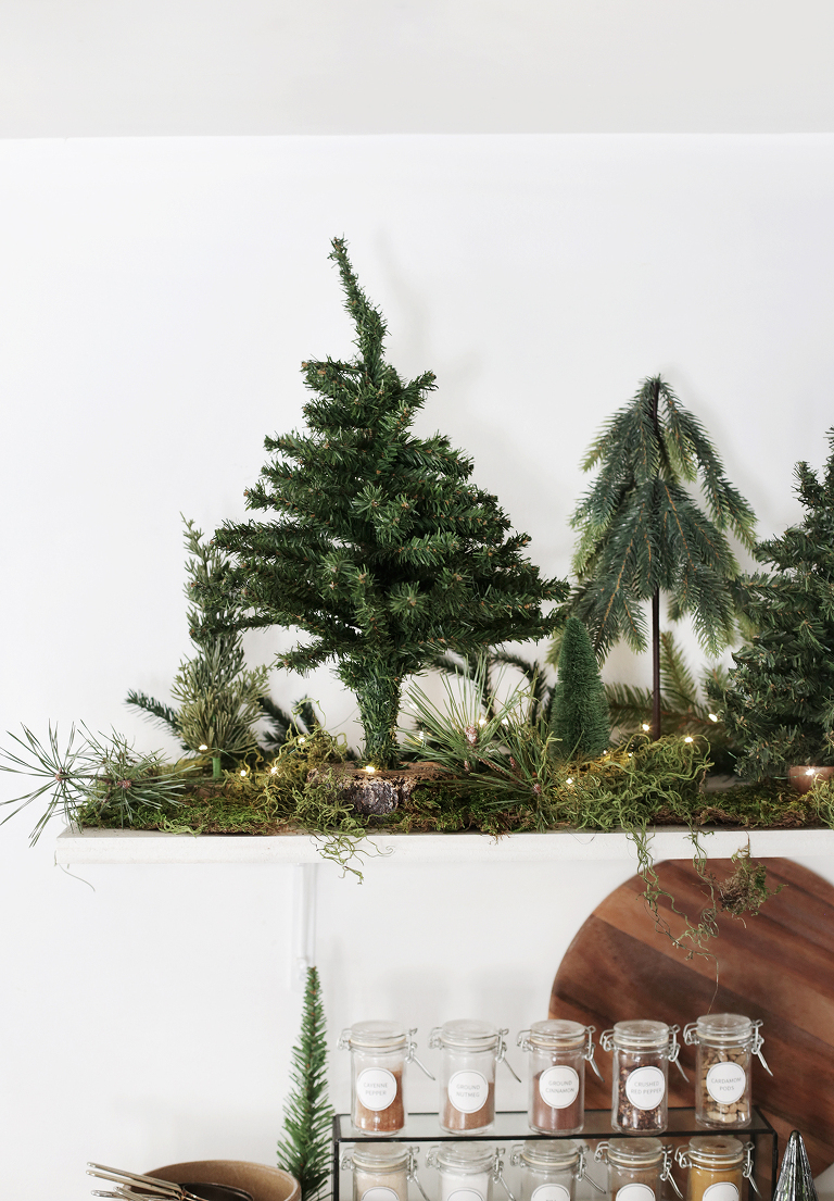 mini pine trees and moss and string lights on white shelf