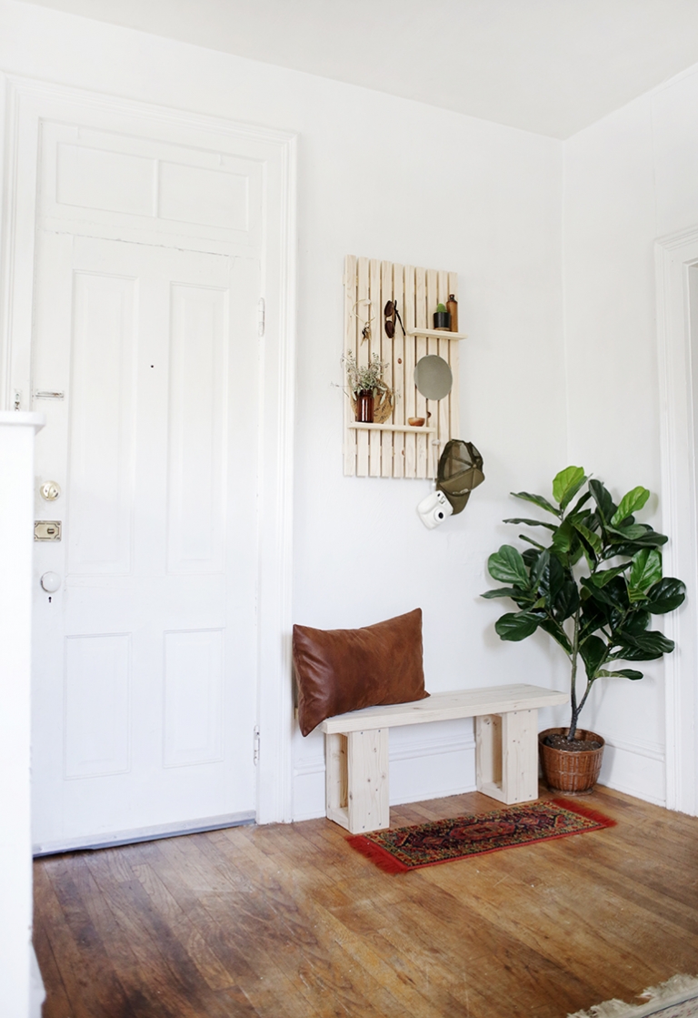 small entryway with wooden bench, wood slat wall shelf, and plant
