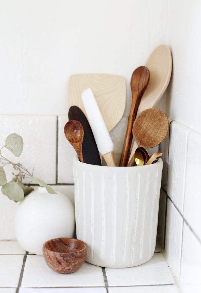 ceramic utensil holder with wooden spoons against white wall
