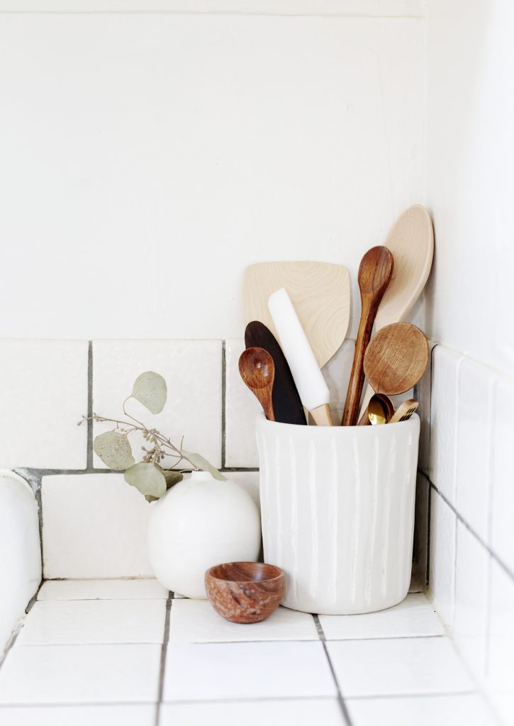 ceramic utensil holder with wooden spoons against white wall