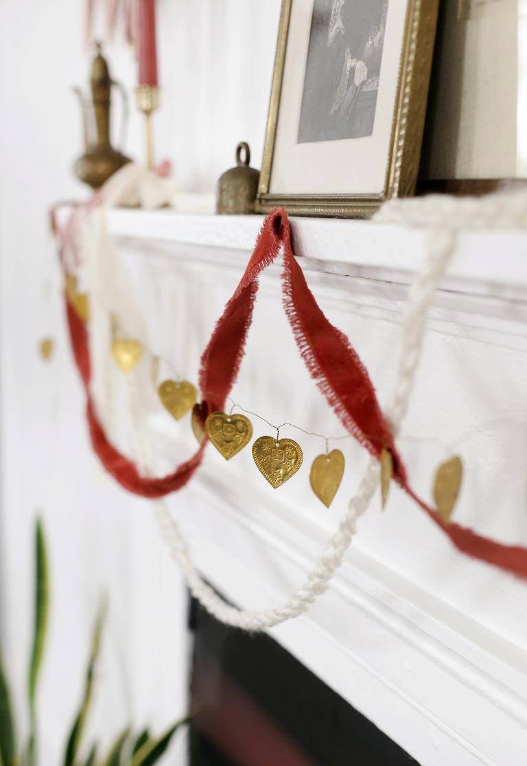 brass heart garland hanging from mantle with yarn and fabric garlands