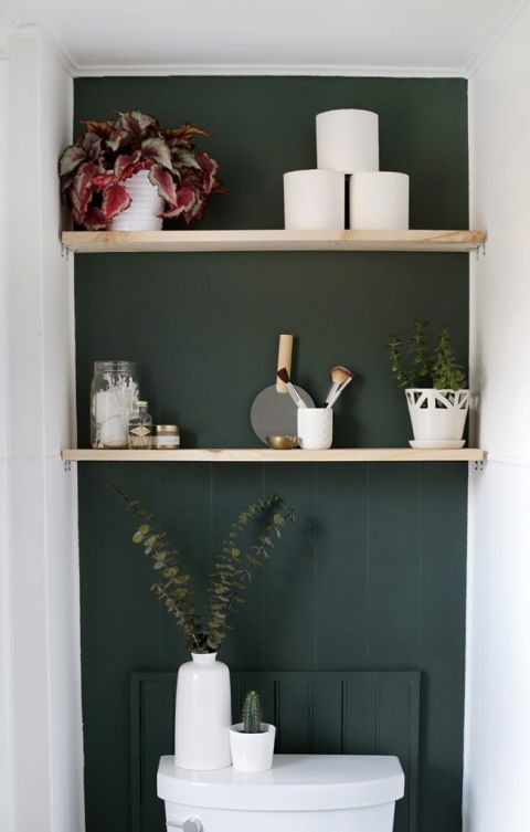 close up of green accent wall with natural wood shelves holding toiletries