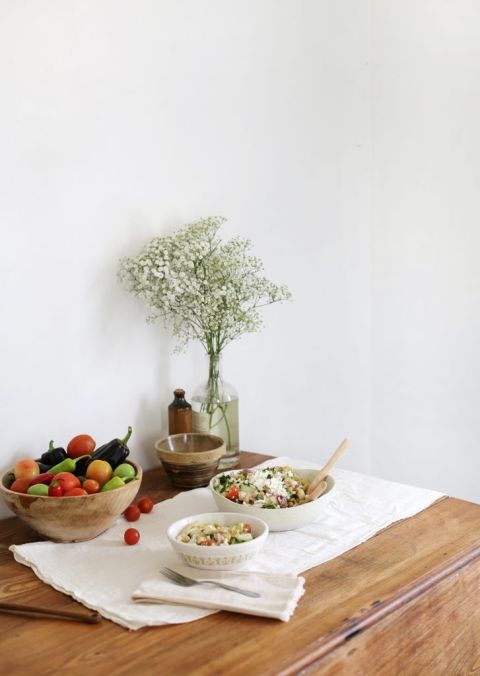 serving dishes on wooden kitchen table with cloth runner and bowl of veggies and decor in background