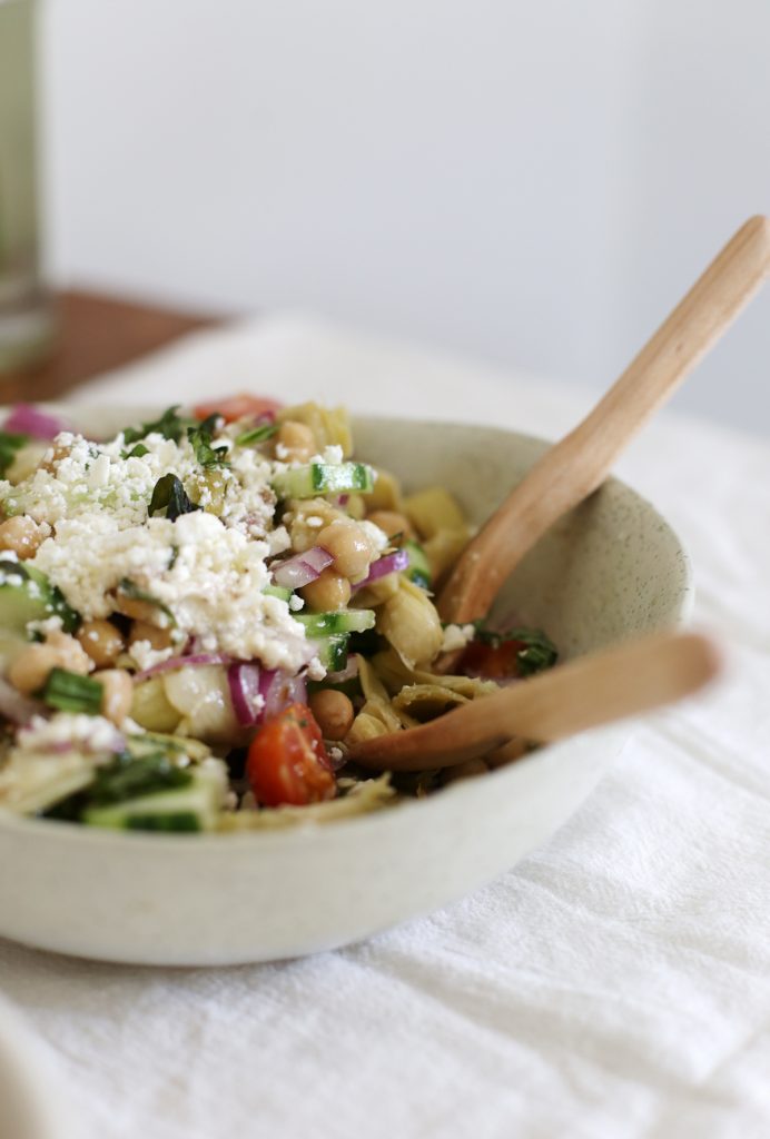 close up of serving dish of artichoke salad with wooden serving utensils