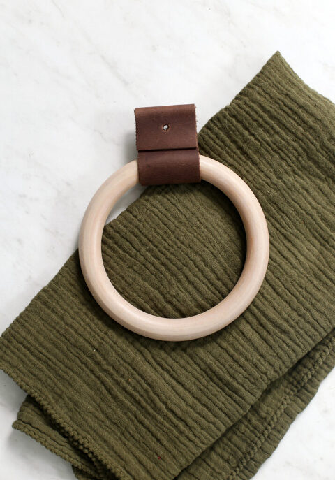 wood and leather towel ring laid on top of green hand towel