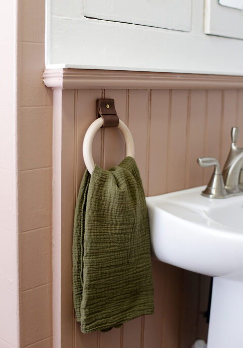 wooden towel ring with green hand towel next to white pedestal sink