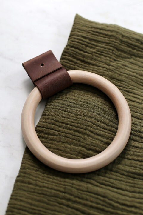 wooden towel ring laying on green hand towel on white marble backdrop