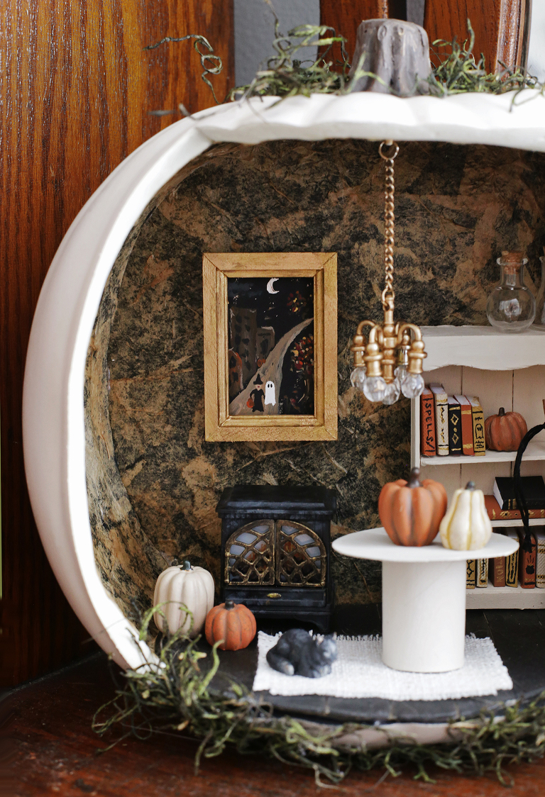 close up of miniature halloween pumpkin house with pumpkins, framed art, fireplace, and chandelier