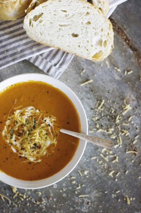 white bowl of red soup with bread lying next to it
