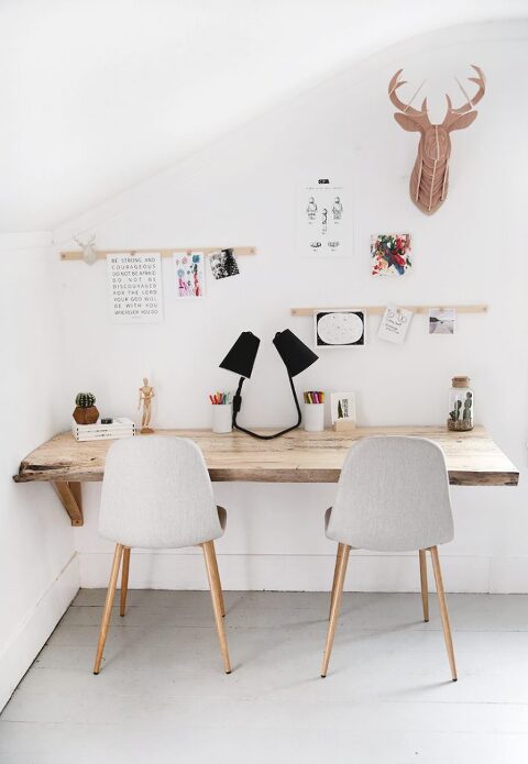 wood desk in bedroom with two chairs at at it with wall hangings and display rail above desk