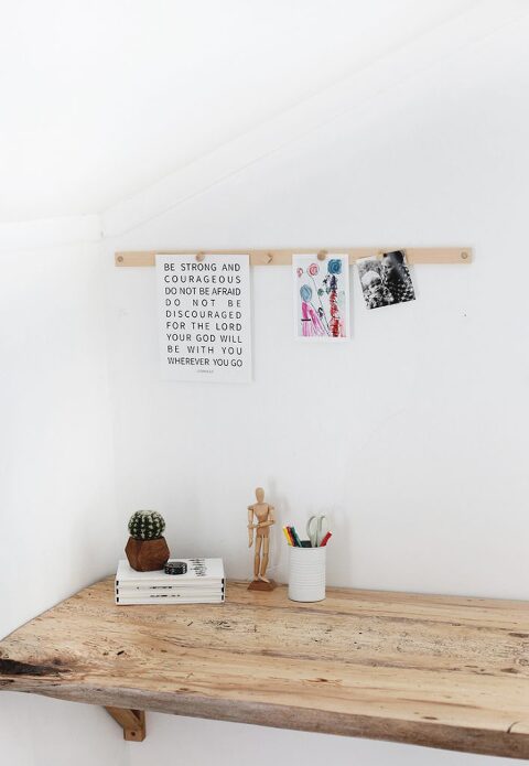 wood desk with wood magnetic display rail above desk with photos and quotes hanging from rail