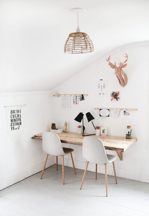 wood desk in bedroom with two chairs at at it with wall hangings and display rail above desk