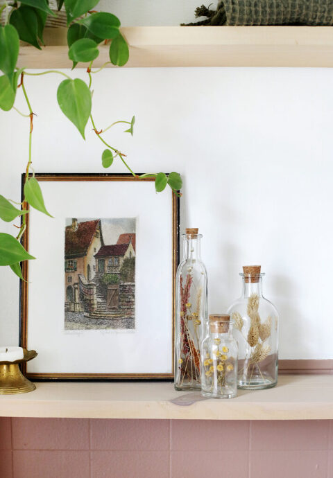 three floral bottles next to small framed artwork on shelf